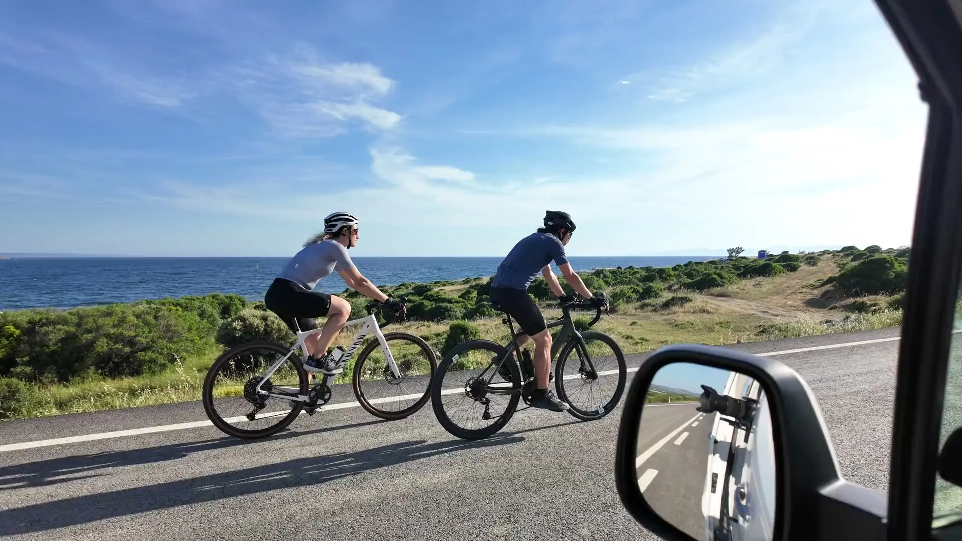 Deniz kıyısındaki yolda pedal çeviren iki bisikletçi